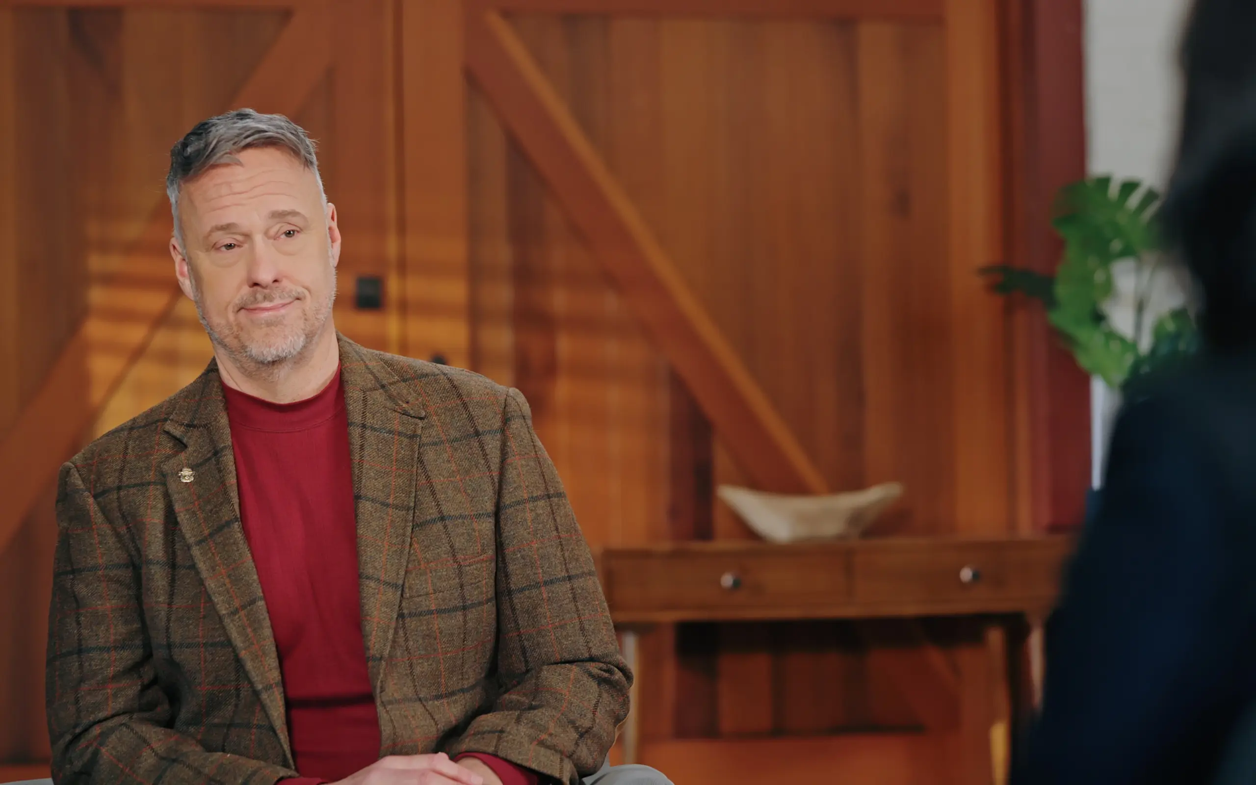 Man in tweed interviewed in a wood-panelled room